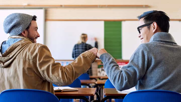 Two friends doing a fist bump in a classroom
