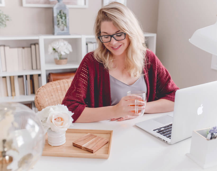 woman at desk with laptop smiling, holding a mug of tea