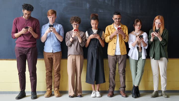 people in a line against a blackboard all looking at their mobile phones