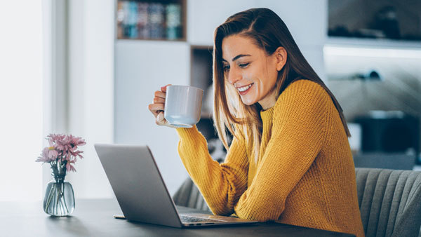 Woman drinking coffee whilst smiling at laptop