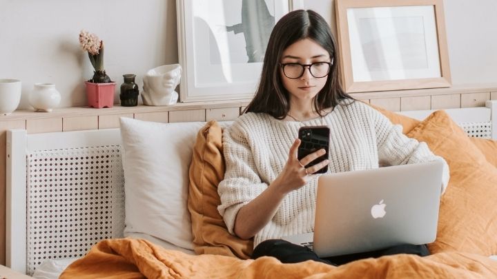 A lady working on a laptop looking at a mobile phone