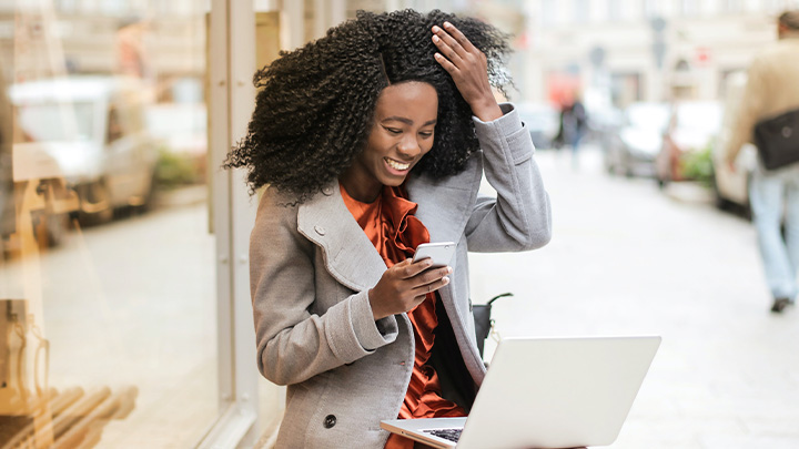 Woman smiling at mobile phone in her hand, with laptop in front of her