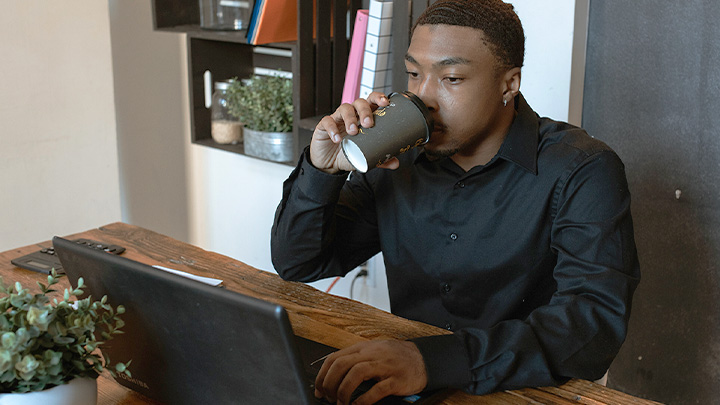 Man working at laptop drinking from a disposable coffee cup