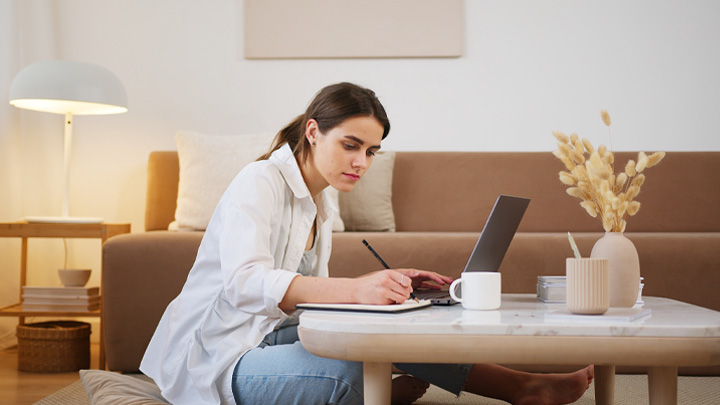 Woman working on laptop while sat on floor at coffee table