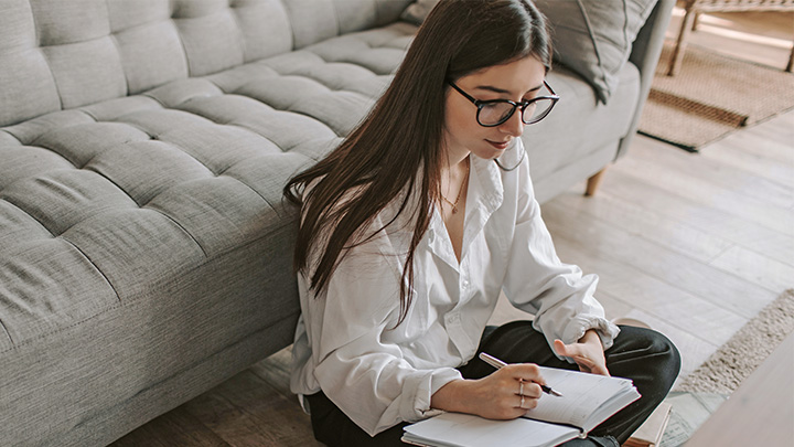 Woman sat on floor writing in notebook