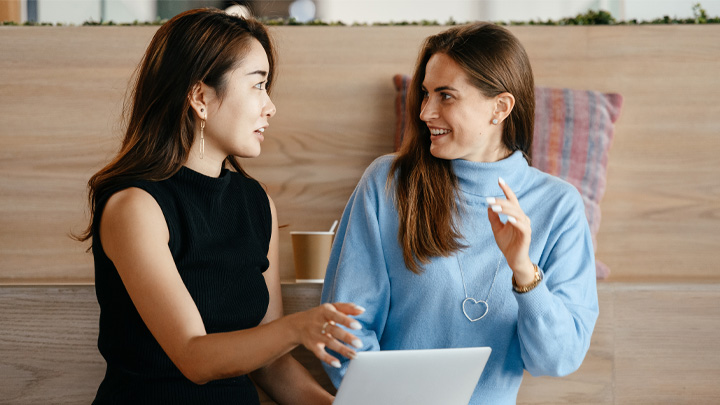 Two women chatting with latop open