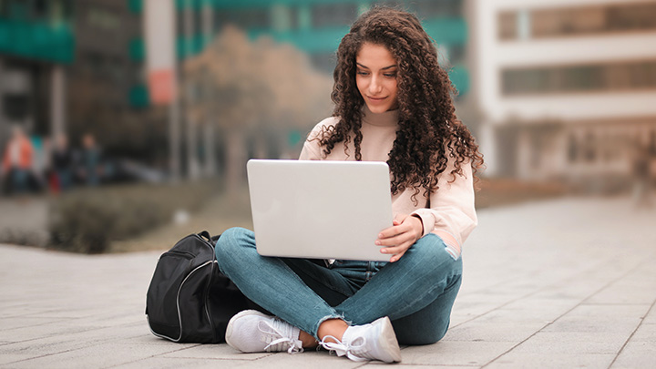 Woman sat outside, crossed legs, working on laptop