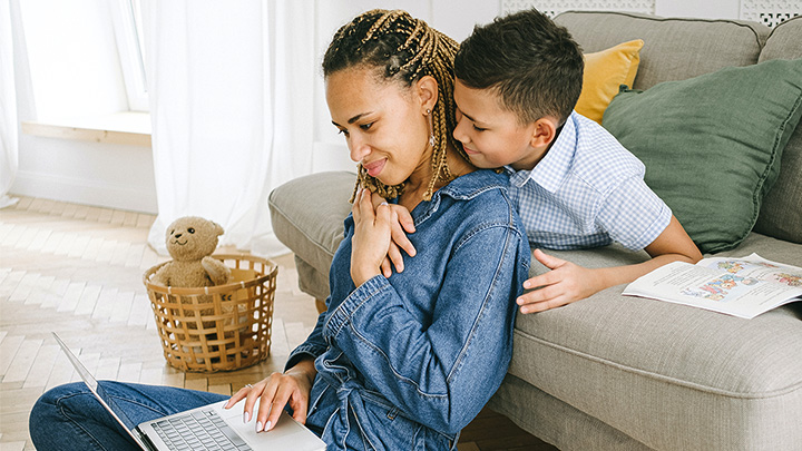 Woman working on laptop with child around her shoulders