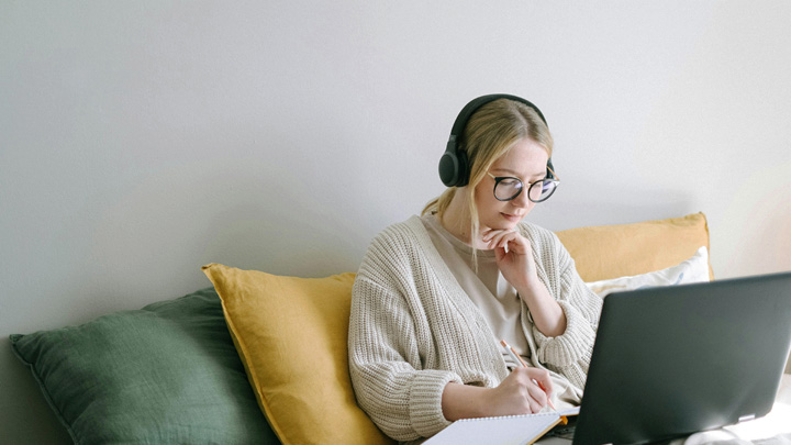 Woman on sofa with headphones on, working at laptop