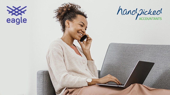 Woman sat on sofa working on a laptop, whilst talking into a mobile phone