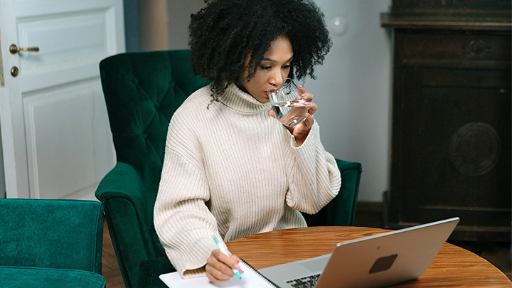 Woman at laptop, drinking water out of a glass