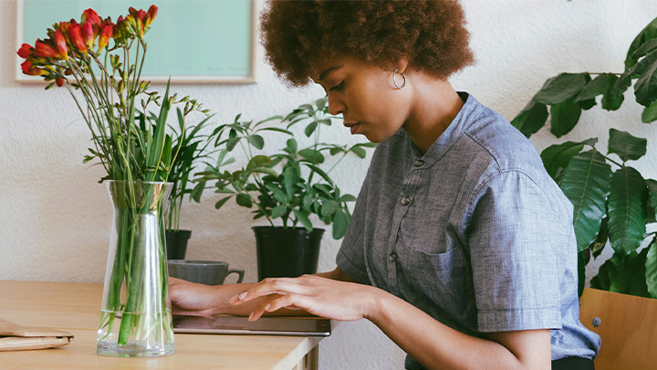 woman working at laptop, next to a vase of flowers