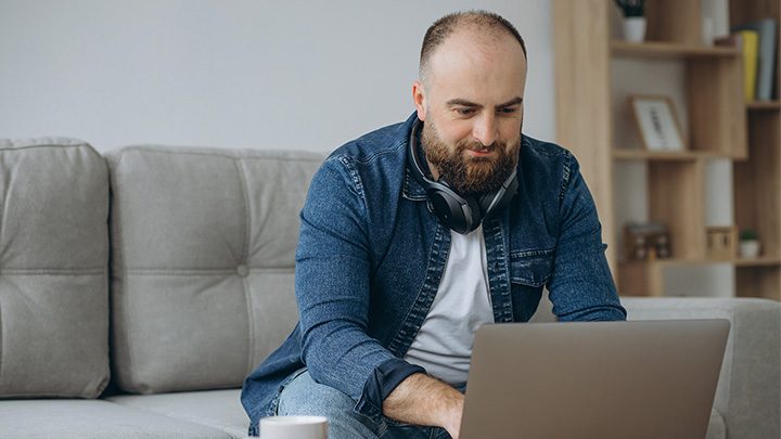 Man sat on sofa, working on a laptop