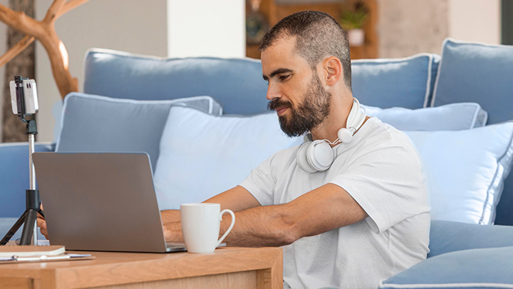 Man sat at coffee table, leaning on sofa, working on a laptop