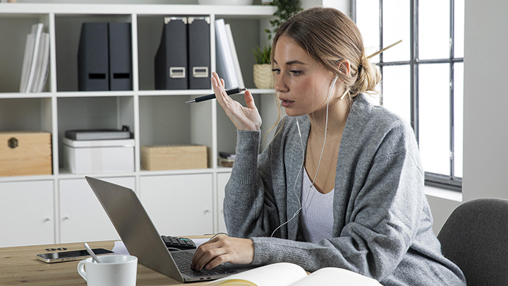 Woman at desk, looking annoyed whilst working on laptop