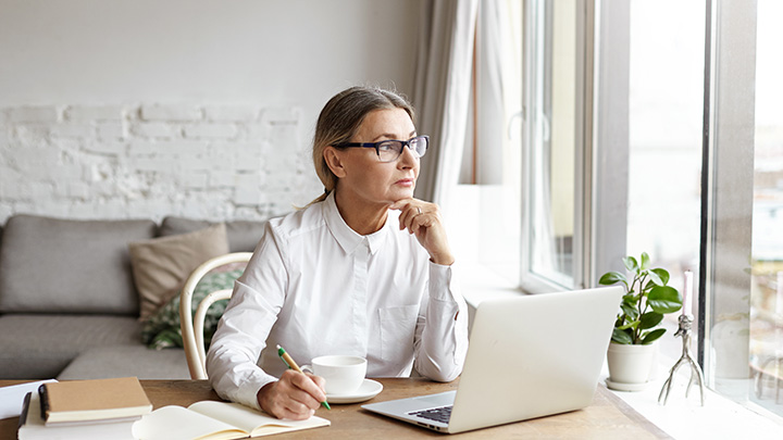 Woman looking out of the window, whilst working on a laptop