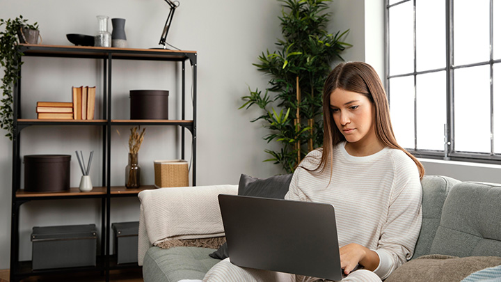 Woman sat at home, on sofa, working on her laptop
