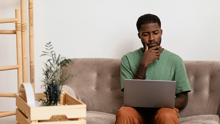 Man working from home, sitting on his sofa, with a laptop on his knee