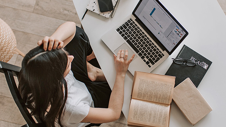 Birds eye view of a woman working at a desk on her laptop, hand to head as if exasperated