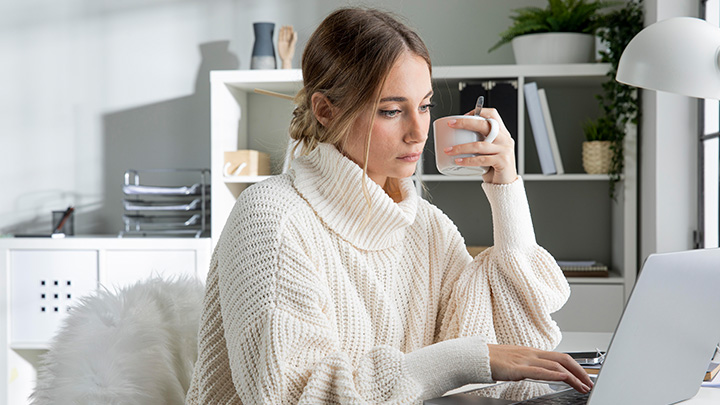 Woman working on a laptop, with a mug in her left hand