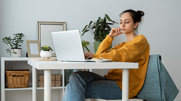 Woman sitting at a desk studying thoughtfully on a laptop